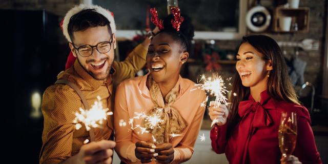 Group of cheerful friends using sparklers and celebrating on New Year's eve at home.