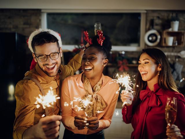 Group of cheerful friends using sparklers and celebrating on New Year's eve at home.