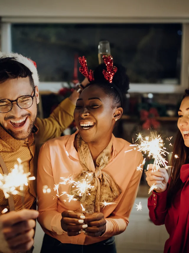 Group of cheerful friends using sparklers and celebrating on New Year's eve at home.